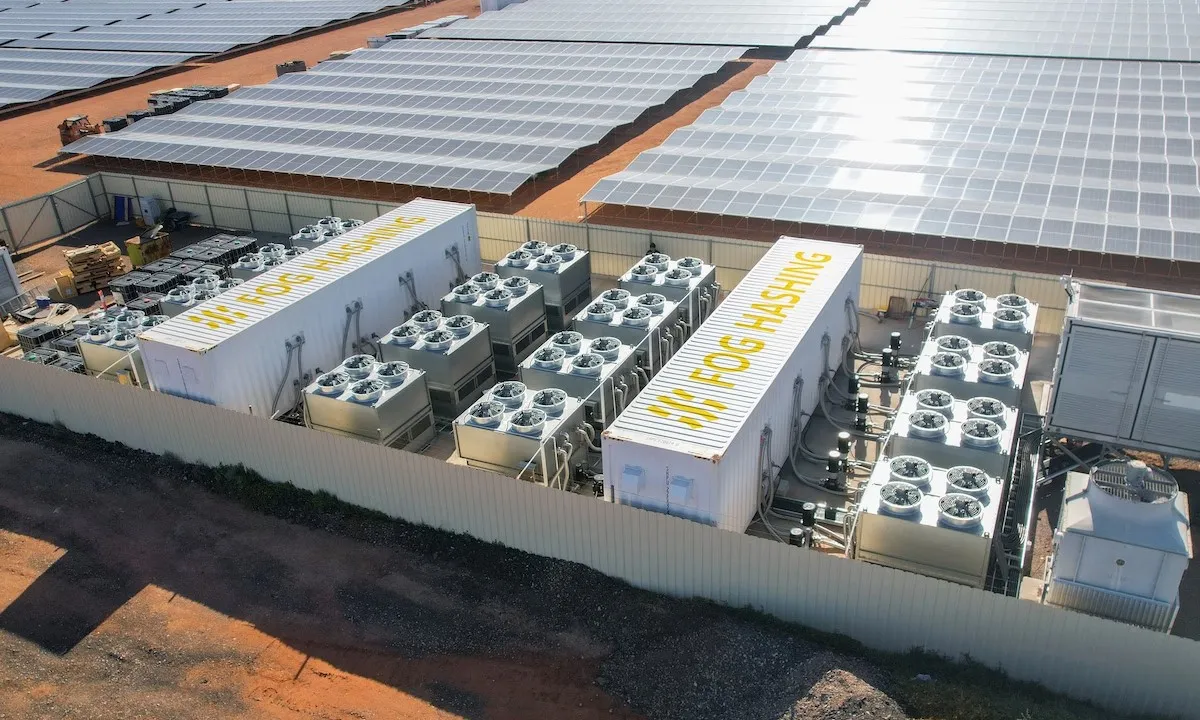 Aerial of Fog Hashing hydro-cooling containers and their dry coolers on a fenced pad beside a utility solar farm
