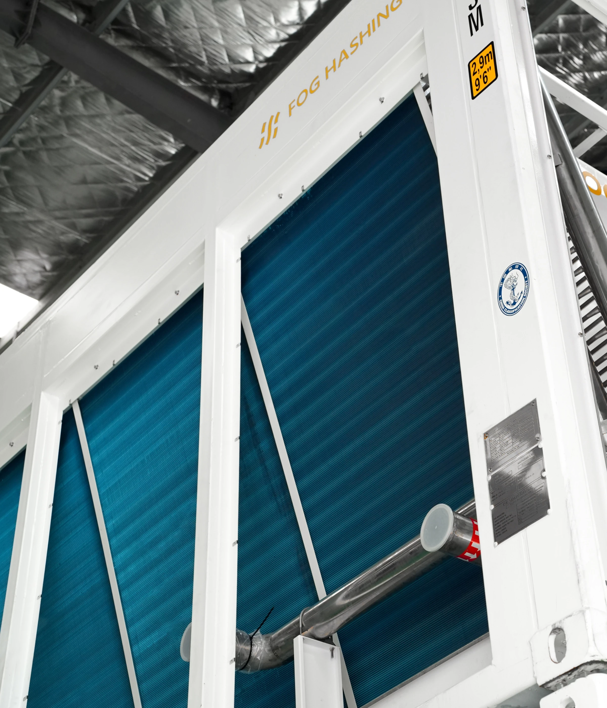 The dry cooler bank on a Fog Hashing hydro container, seen from below: blue fin blocks behind the white frame, the classification-society plate and nameplate alongside