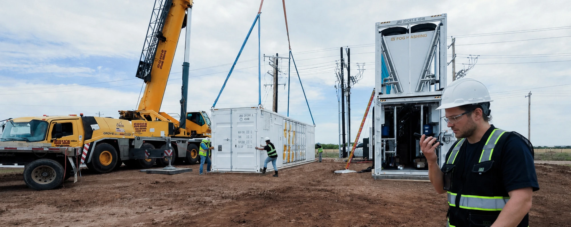 A crane setting an HC40 container beside an open Fog Hashing unit on site, a technician on the radio in the foreground