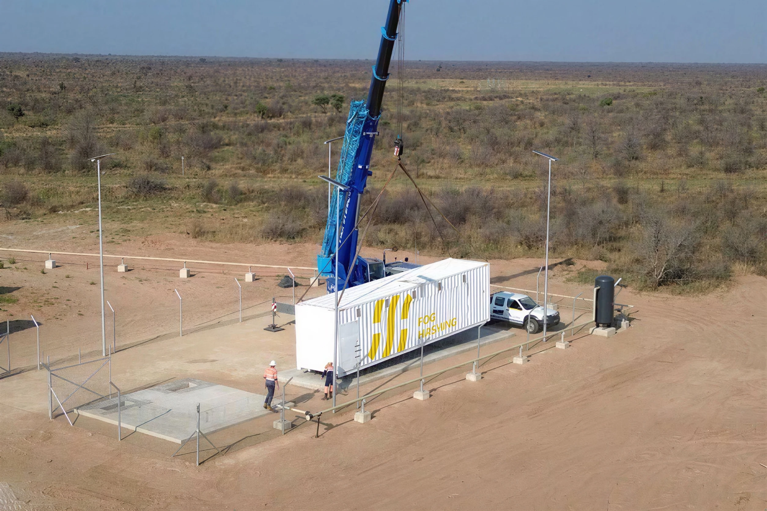 Aerial of a Fog Hashing container craned onto its pad at a savanna site in Africa, crew guiding it down