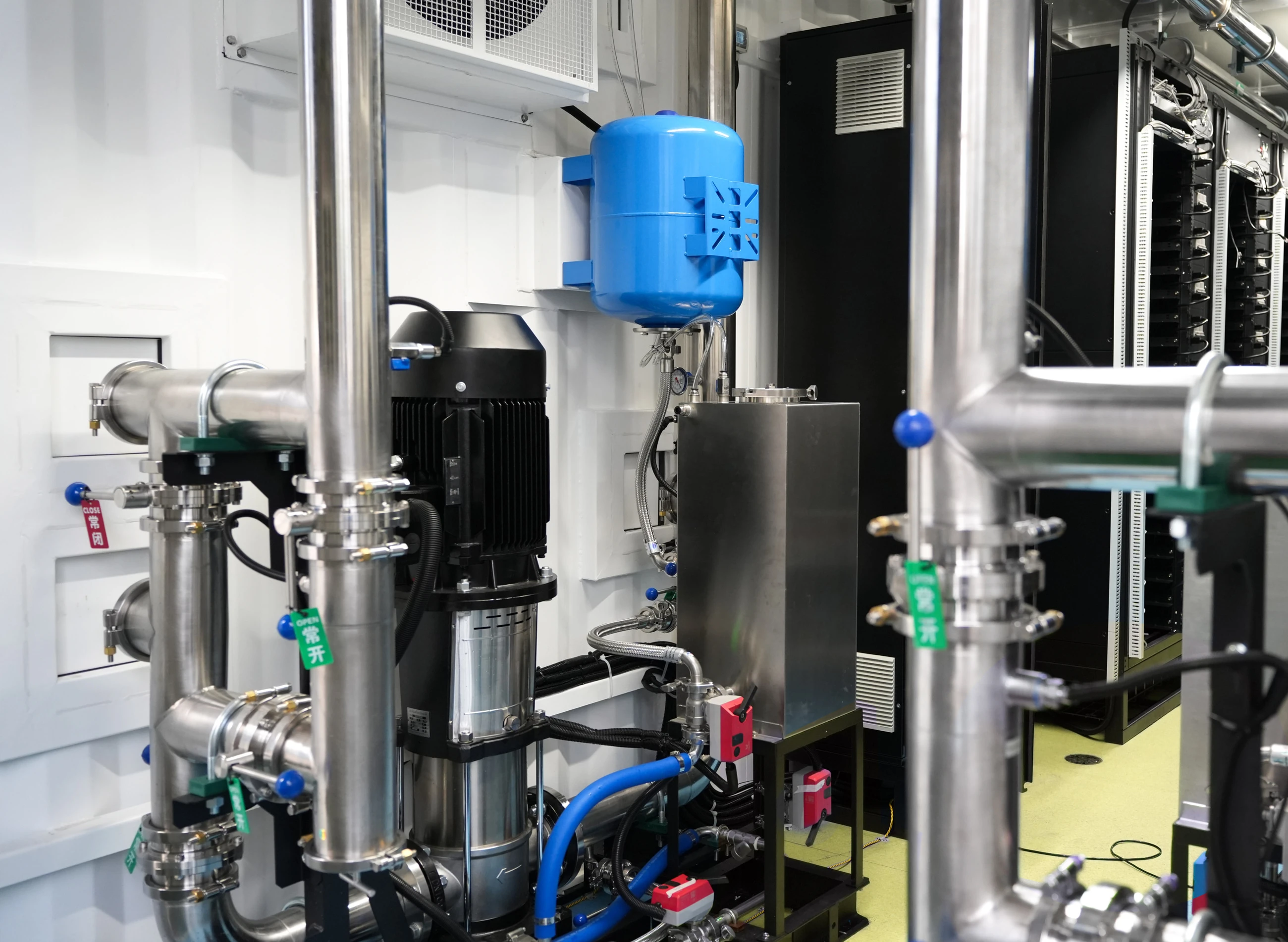Inside the CDU: circulation pump, stainless distribution piping and the expansion tank above it