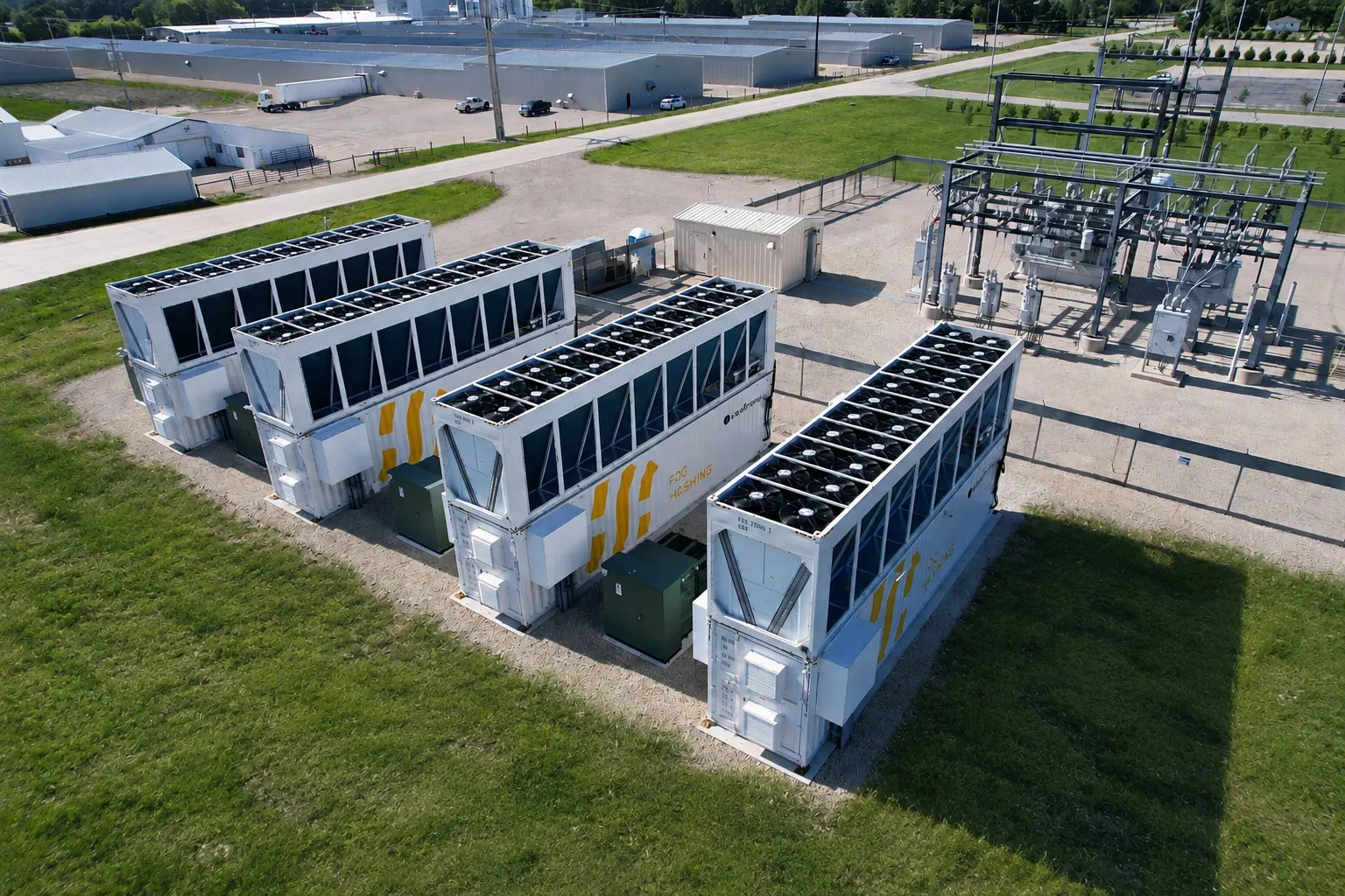 Four Fog Hashing hydro cooling units on their pads beside the site substation, seen from the air