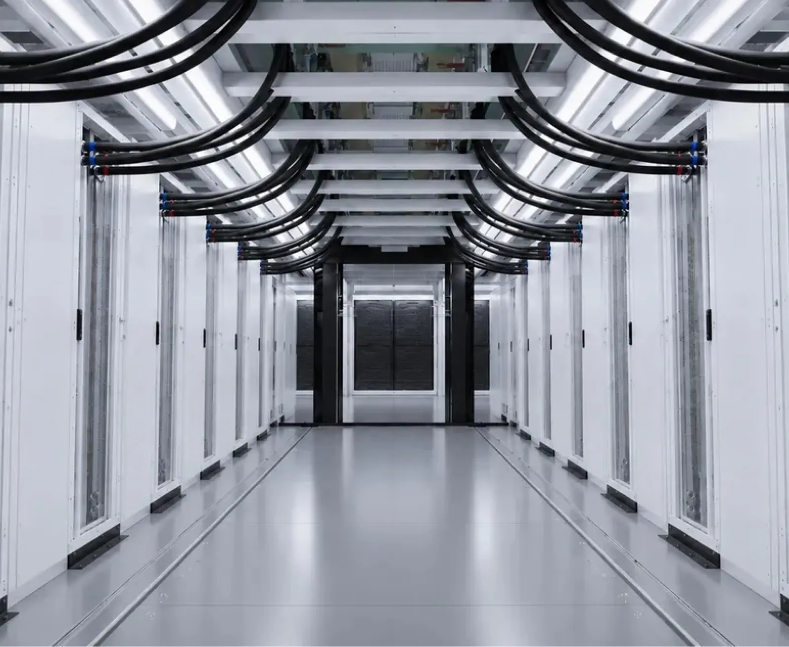 Aisle of a white-paneled data hall, power cabling dropping from the overhead tray into each cabinet