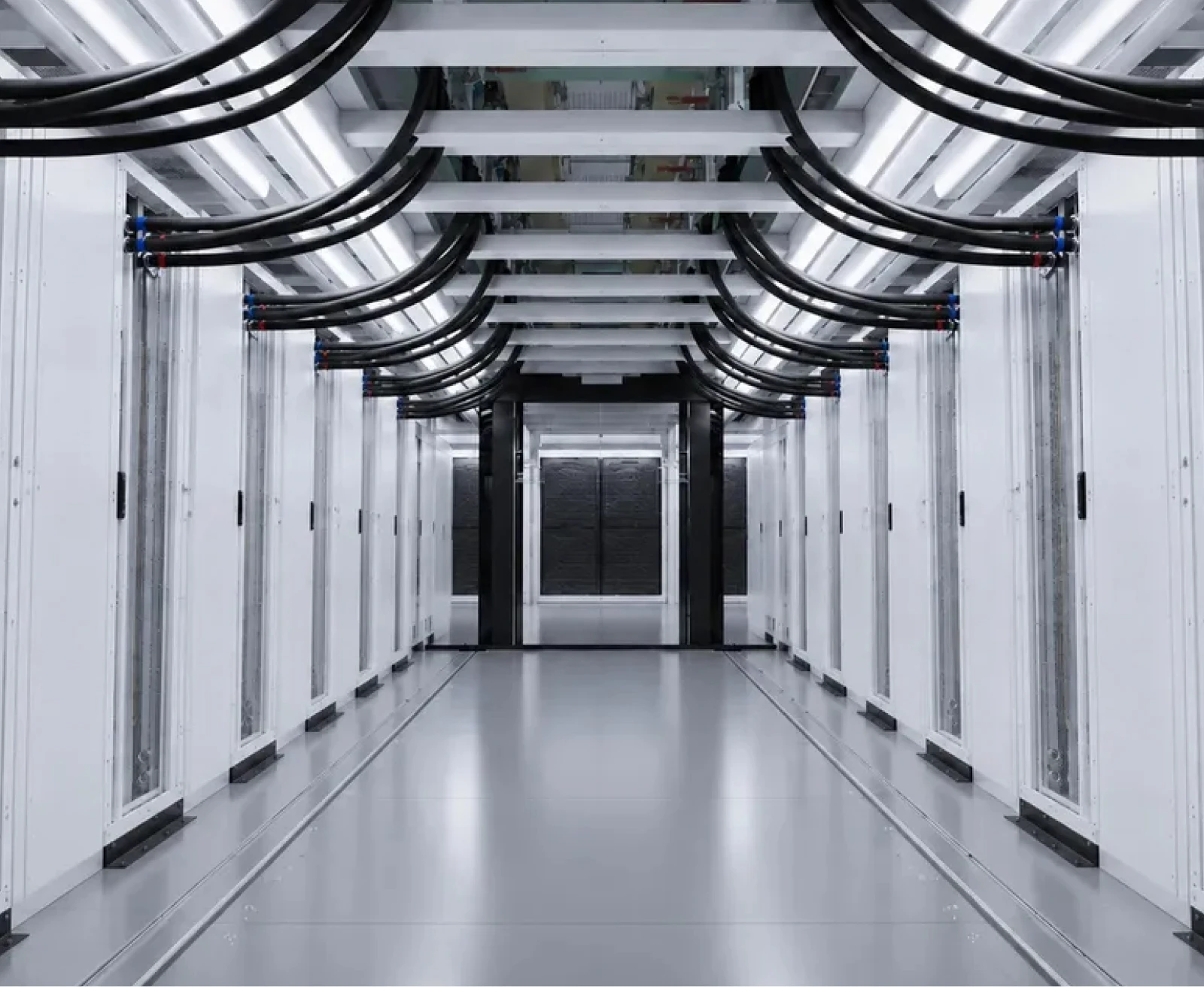 Aisle of a white-paneled data hall, power cabling dropping from the overhead tray into each cabinet